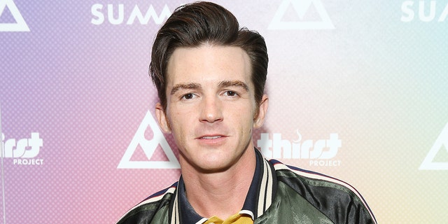 Drake Bell wears a green jacket and yellow under shirt with a blue striped collar on the red carpet