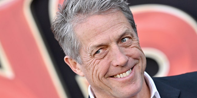 Hugh Grant looks to his right off-camera and smiles almost devilishly on the red carpet in Los Angeles