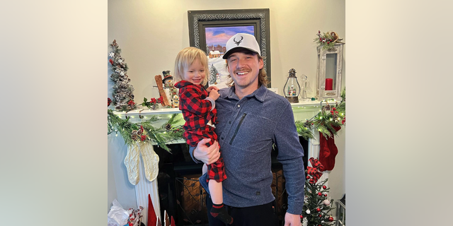 Morgan Wallen holds his son Indigo in front of Christmas decorations