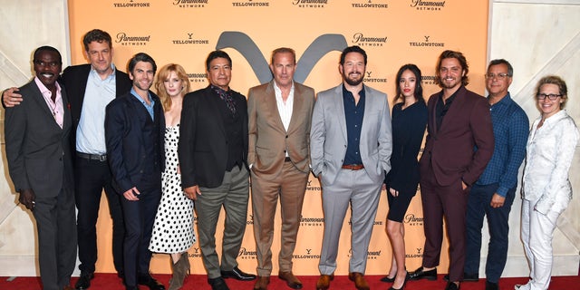 "Yellowstone" cast on the red carpet centered by Kevin Costner in a tan suit and white shirt in front of an orange "Yellowstone" backdrop