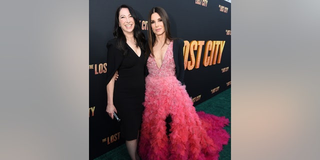 Gasine Bullock-Prada in a black dress smiles on the red carpet next to sister Sandra Bullock in a beautiful pink dress with a feather train on the carpet for the premiere of "The Lost City"