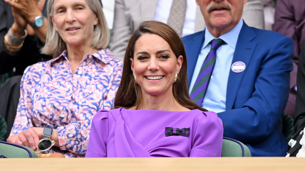 Kate Middleton smiles while seated at Wimbledon in a purple dress