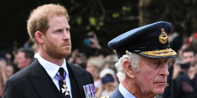 Prince Harry looking somber in a morning suit with medal as he walks behind King Charles in a military uniform