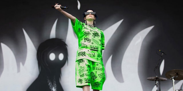 Billie Eilish holds her microphone out to the audience in a green matching shorts and t-shirt set in Middlesbrough, England