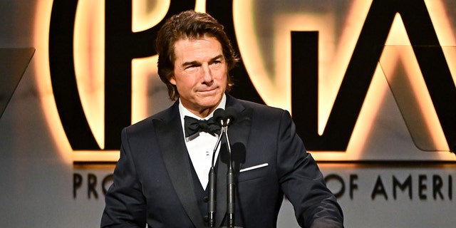 Tom Cruise on stage in a classic tuxedo behind the podium at the Producers Guild Awards