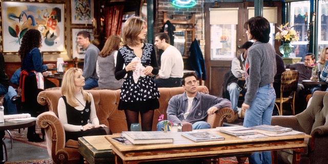 Phoebe (Lisa Kudrow) and Joey (Matt LeBlanc) sit on the orange couch while Rachel (Jennifer Aniston) looks at Monica (Courteney Cox) during a scene from "Friends"