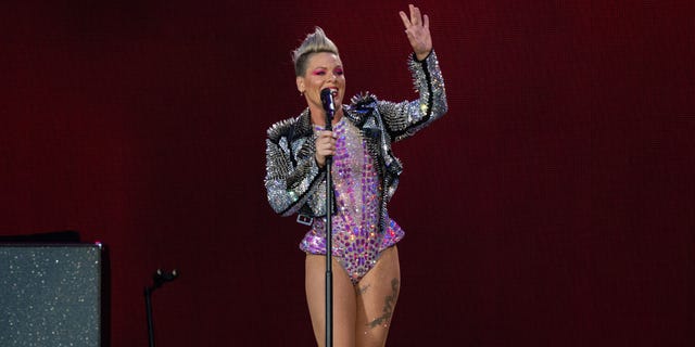 Pink in a purple sparkly bodysuit and silver jacket waves to fans while on stage in London