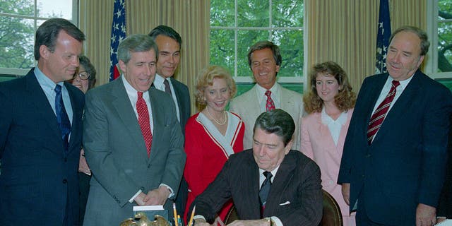 Members of the National day Prayer organizing committee looking on, including entertainer Pat Boone, (C-white suit), President Reagan signs a proclamation honoring the day in an oval office ceremony May 5th.