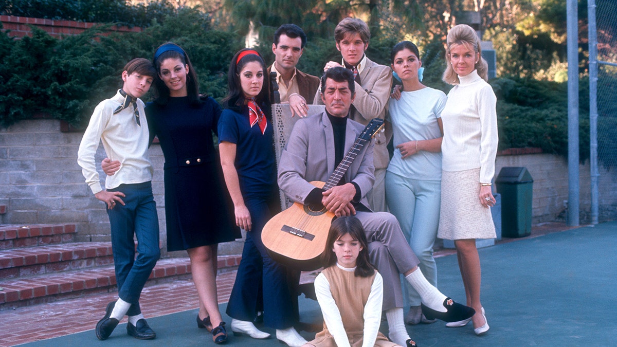 Dean Martin surrounded by his children as he holds a guitar.