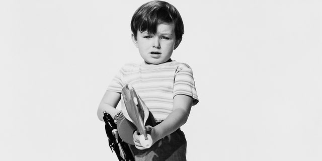 A young Jerry Mathers wearing a striped shirt and holding a toy