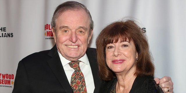 Jerry Mathers in a suit and tie smiling next to his wife