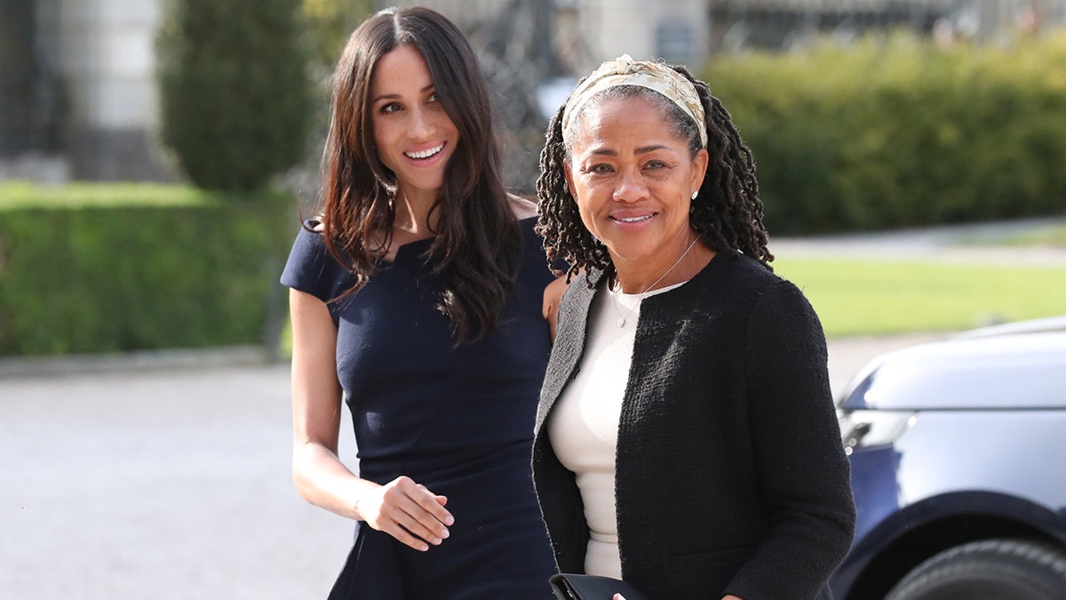 Meghan Markle wearing a navy blue dress next to her mother Doria Ragland wearing a black blazer and a white dress