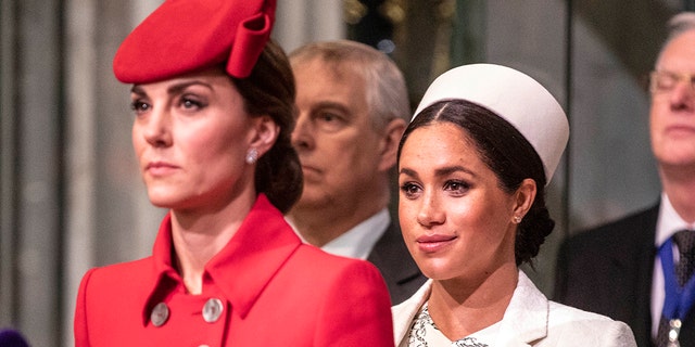 A close-up of Kate Middleton in a red dress and a matching hat next to Meghan Markle in a white dress with a matching hat