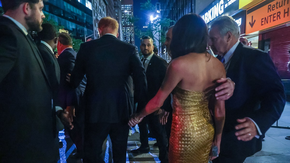 Meghan Markle in a gold dress being escorted by security