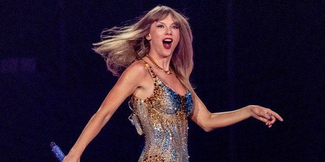 A close-up of Taylor Swift wearing a sparkling costume on stage while she holds a mic