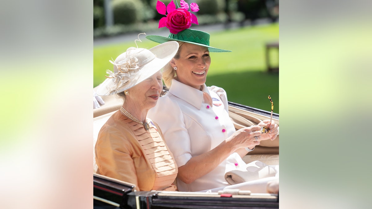 Zara Tindall smiling wearing a white suit dress sitting next to her mother on a royal carriage.