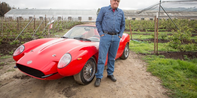Jay Leno poses with a red sports car for his show about rare vehicles