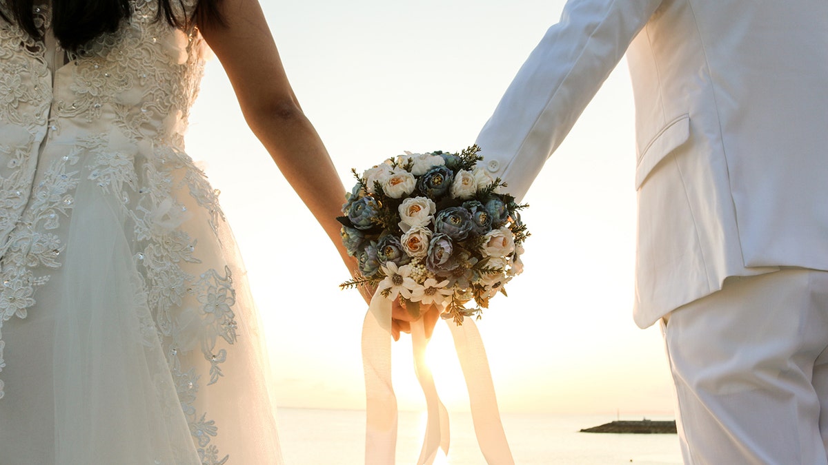 Bride and groom with their backs to the camera holding a bouquet of flowers