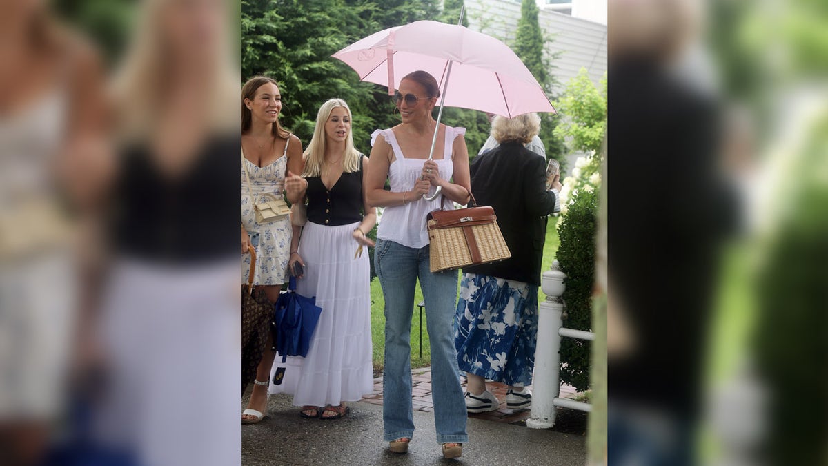 Singer Jennifer Lopez holds pink umbrella in the rain.