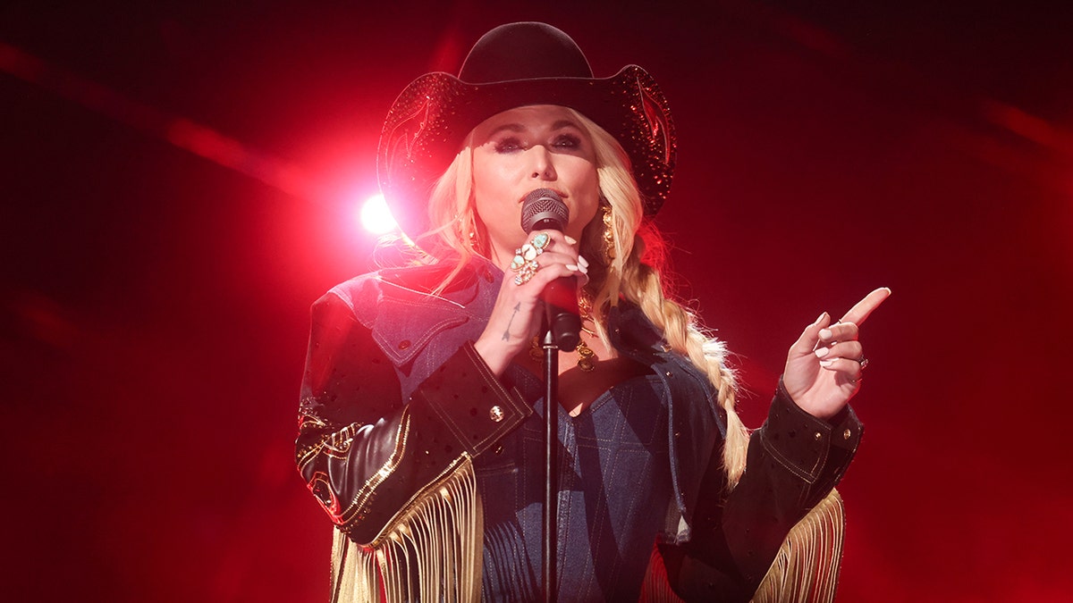 Miranda Lambert sings into the microphone wearing a fringe jean outfit and black hat