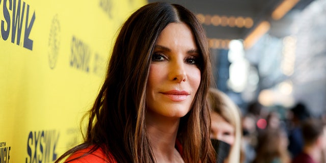 Sandra Bullock looks slightly back at the camera in bright orange dress at SXSW